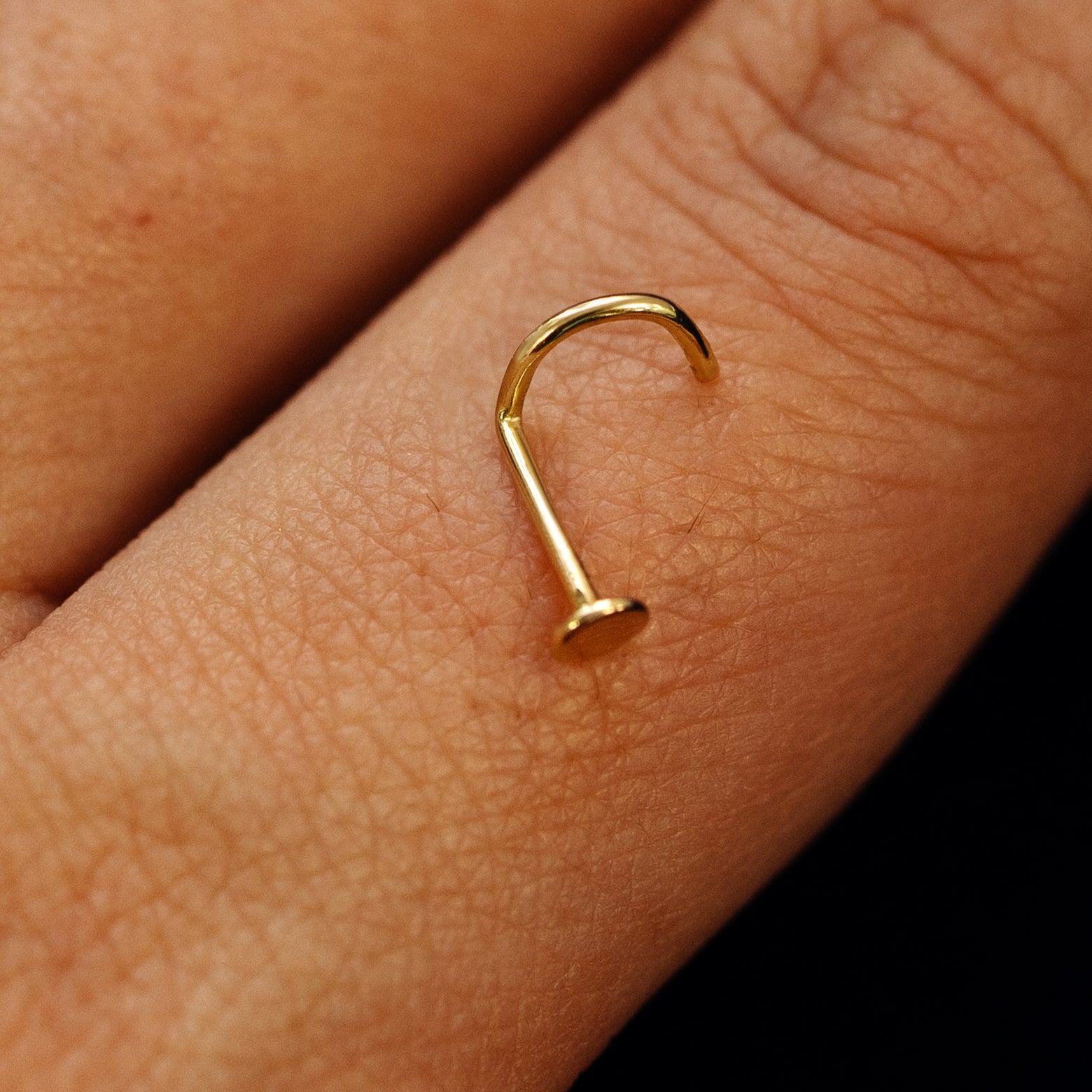 Close up view of a single 14k solid gold Circle Nose Stud with a twist corkscrew backing resting on the back on a model's hand