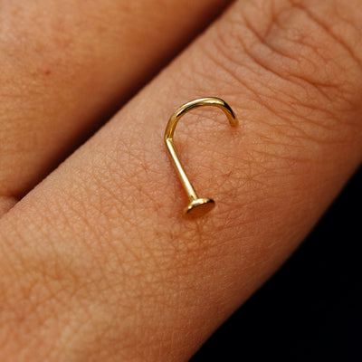 Close up view of a single 14k solid gold Circle Nose Stud with a twist corkscrew backing resting on the back on a model's hand