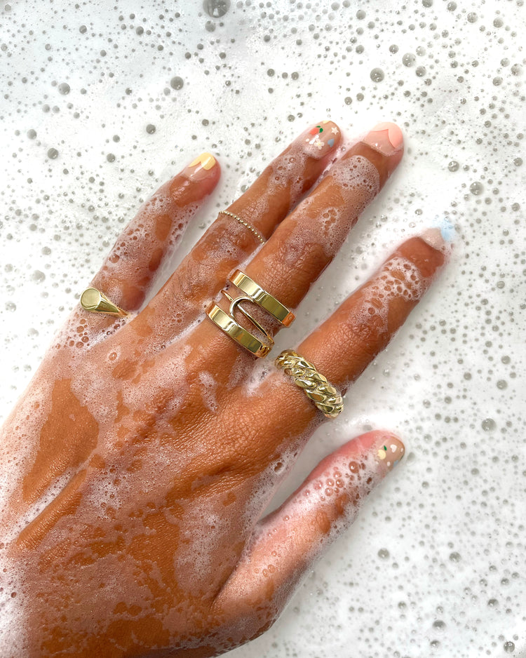 close up view of a hand in soapy water wearing various Automic Gold solid yellow gold rings 