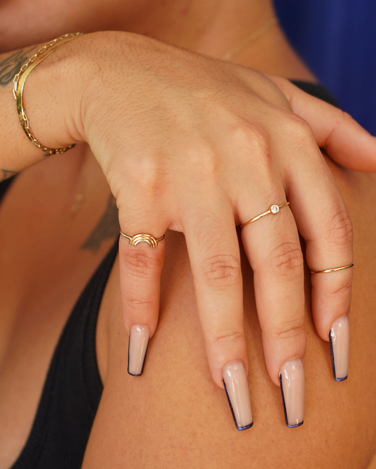 A model with long nails is gripping their shoulder while wearing a Diamond Ring and a Rainbow Ring
