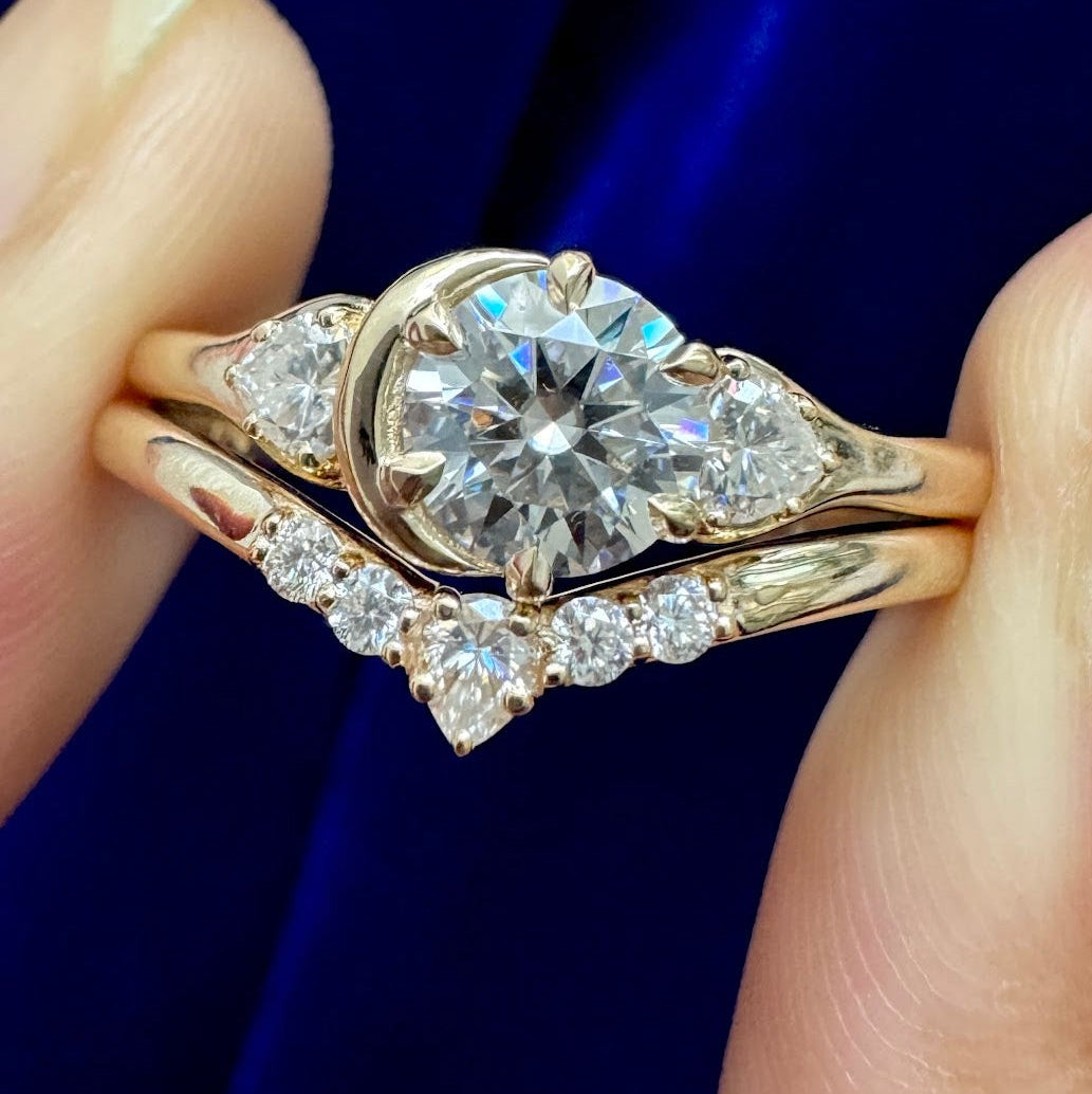 A 14k  gold moissanite engagement ring with a crescent moon and sun design and its matching chevron stacking wedding band