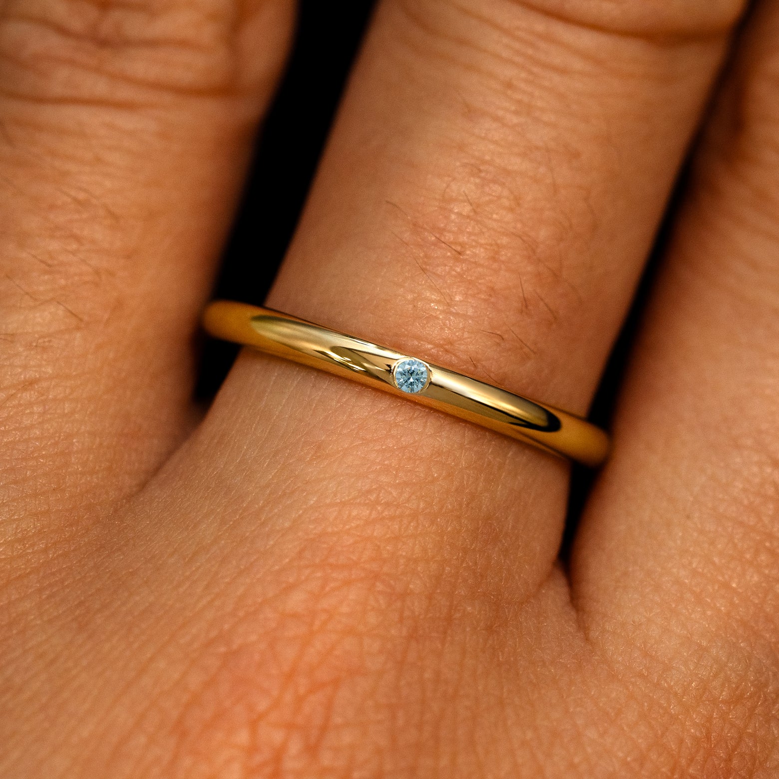 A 14k yellow gold Flush Set Round Light Blue Diamond Ring on a model's finger