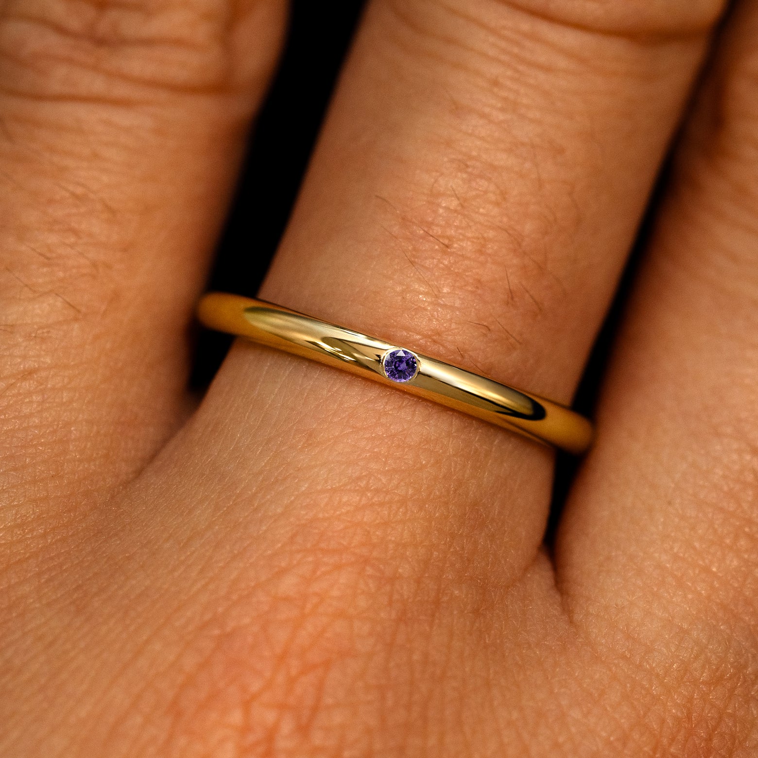 A 14k yellow gold Flush Set Round Purple Sapphire Ring on a model's finger