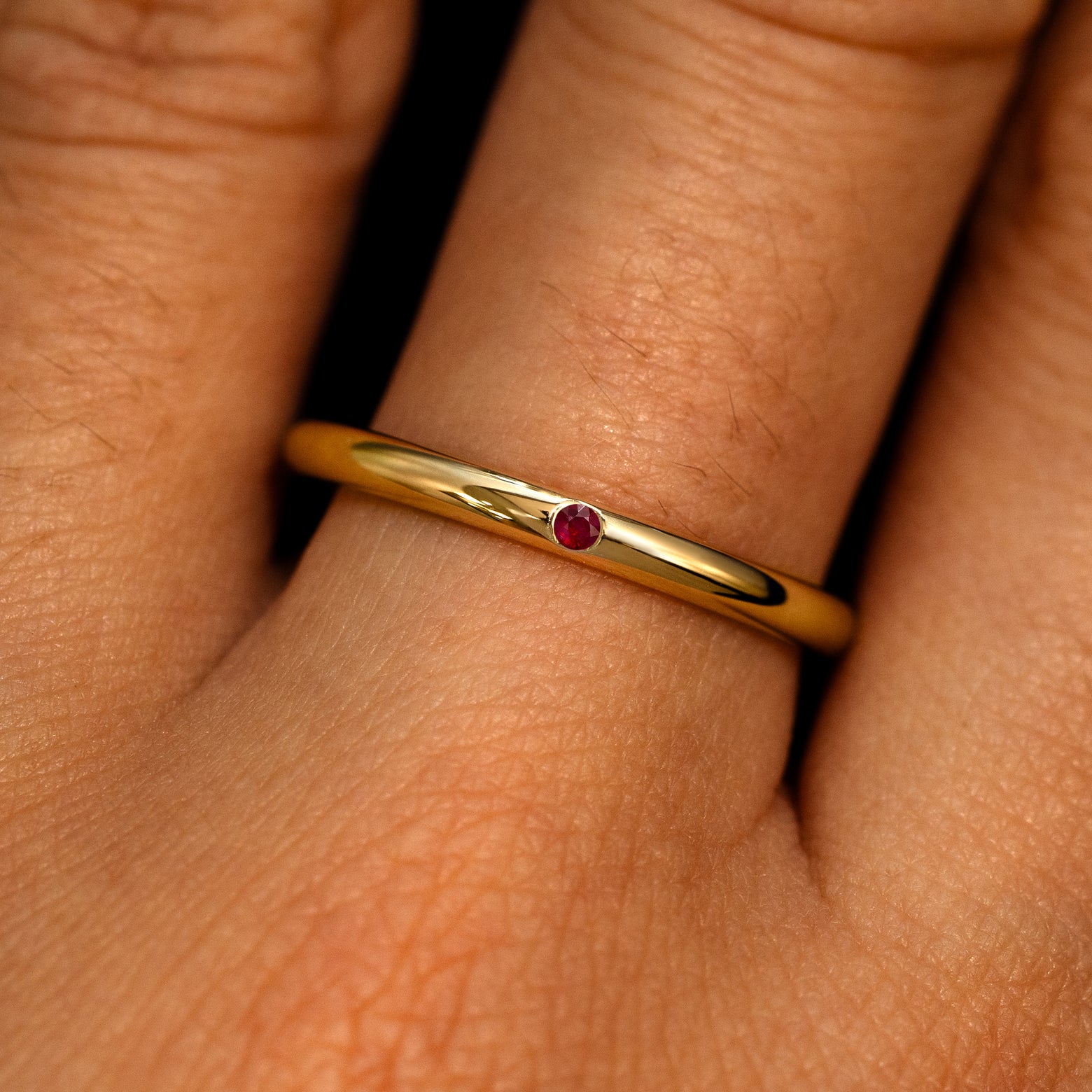 A 14k yellow gold Flush Set Round Ruby Ring on a model's finger