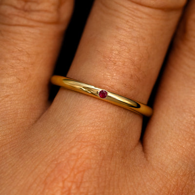 A 14k yellow gold Flush Set Round Ruby Ring on a model's finger