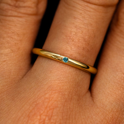 A 14k yellow gold Flush Set Round Teal Sapphire Ring on a model's finger