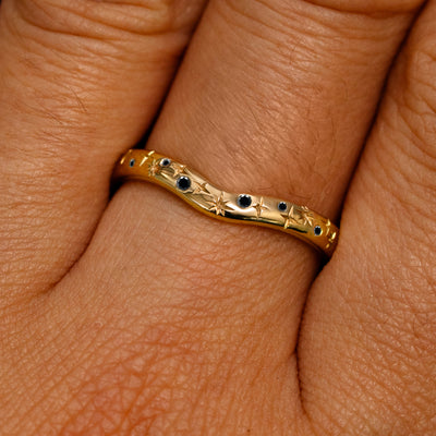 Close up view of a model's fingers wearing a 14k yellow gold Curvy Chevron Black Diamond Stars Band