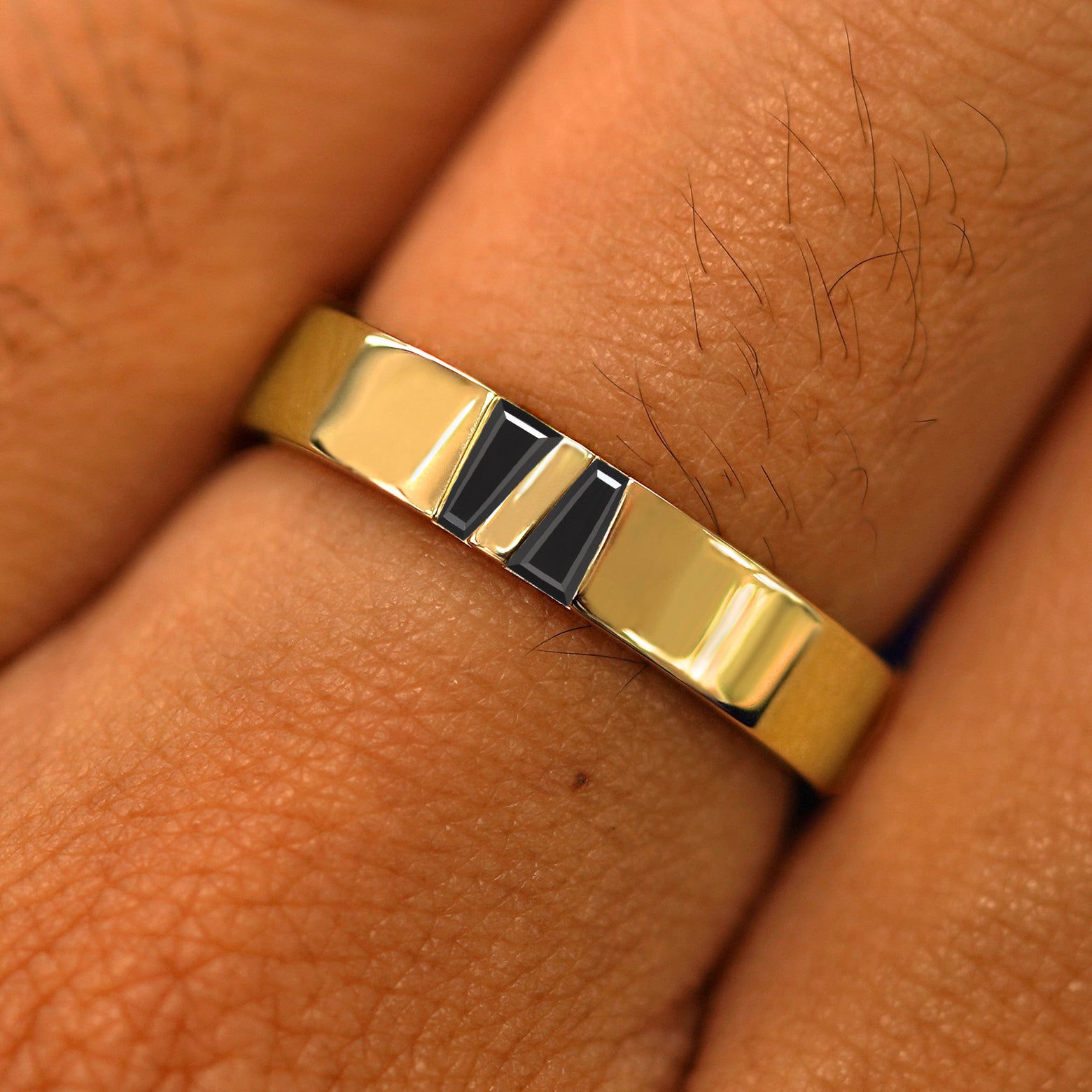 Close up view of a model's hand wearing a solid yellow gold Double Baguette Black Diamond Band