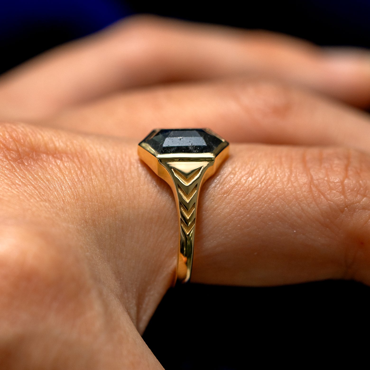 Side view of a model's finger wearing a solid 14k gold Chronos Ring to show the engravings