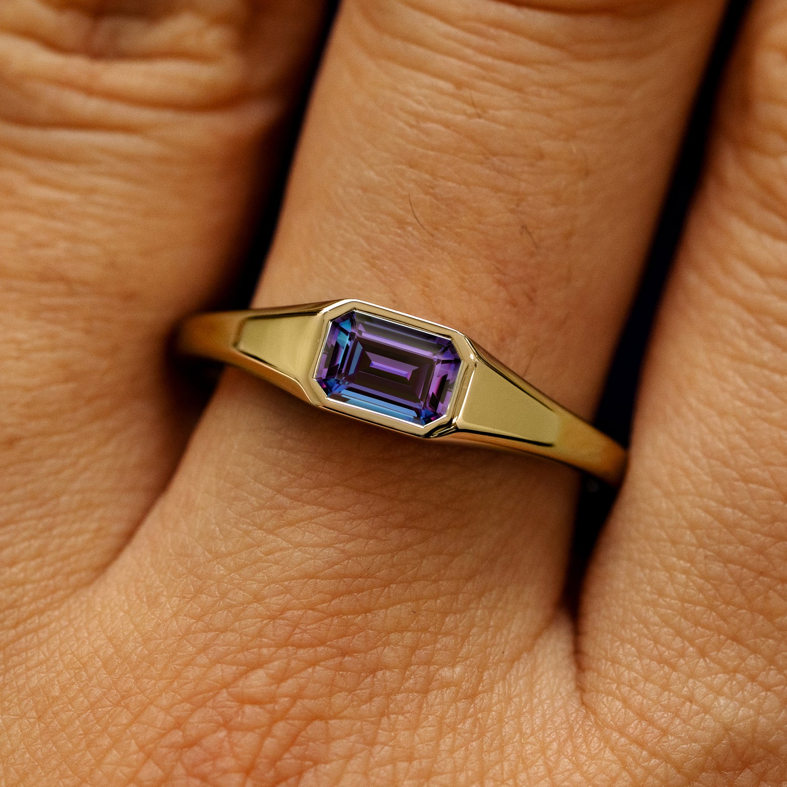 Close up view of a model's fingers wearing a 14k yellow gold Emerald Cut Lab Created Alexandrite Signet Ring