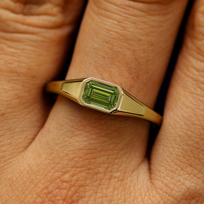 Close up view of a model's fingers wearing a 14k yellow gold Emerald Cut Green Lab Created Diamond Signet Ring