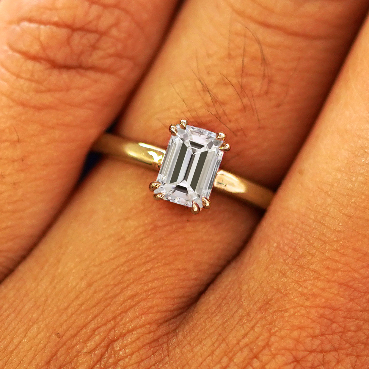 Close up view of a model's fingers wearing a 14k yellow gold Emerald Cut Lab Diamond Ring