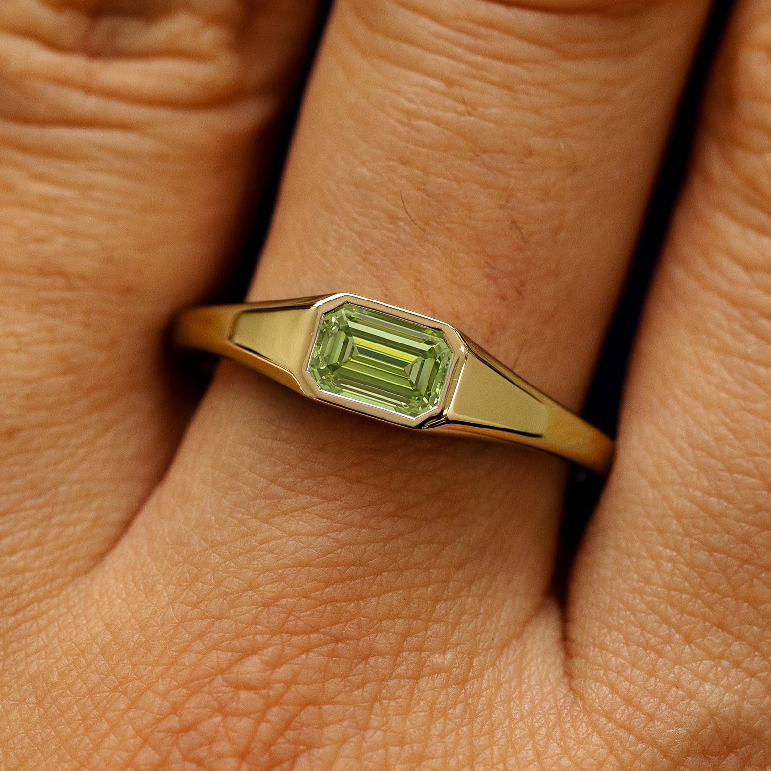Close up view of a model's fingers wearing a 14k yellow gold Emerald Cut Green Lab Created Diamond Signet Ring
