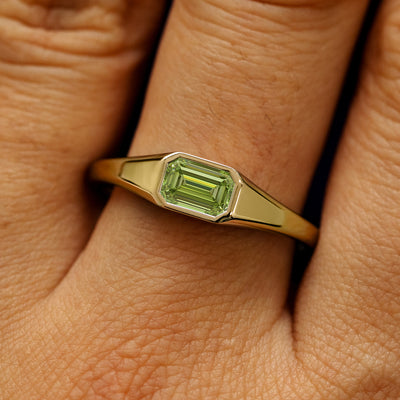 Close up view of a model's fingers wearing a 14k yellow gold Emerald Cut Green Lab Created Diamond Signet Ring