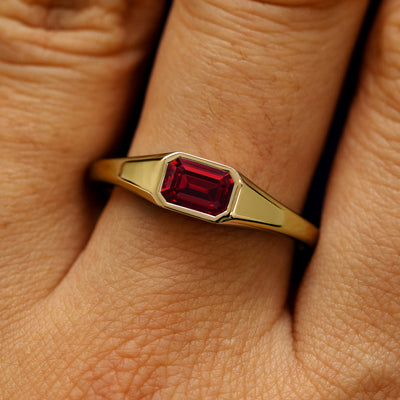 Close up view of a model's fingers wearing a 14k yellow gold Emerald Cut Lab Created Ruby Signet Ring