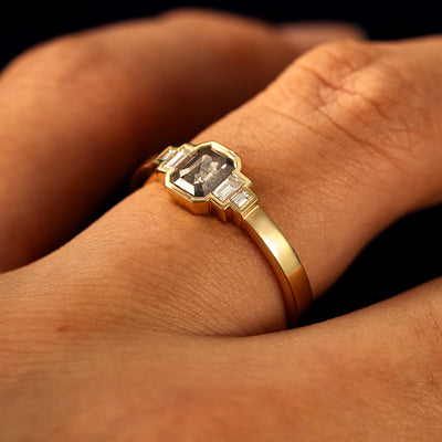 Side view of a solid 14 karat gold Emerald Cut Salt and Pepper and Clear Baguette Diamond Ring on a model's finger