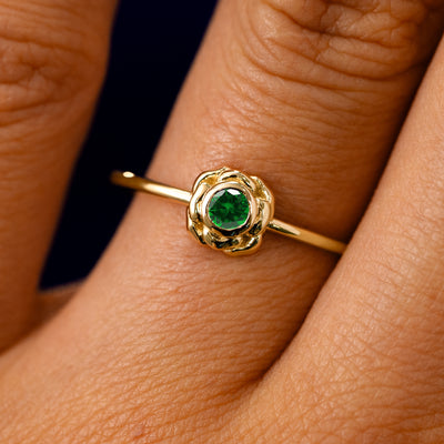 A solid 14k yellow gold Emerald Gemstone Flower Ring on a model's finger