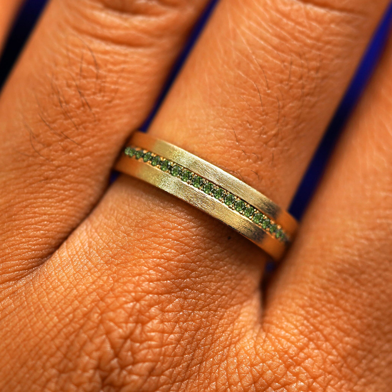 Close up view of a model's fingers wearing a 14k yellow gold Endless Green Diamond Band