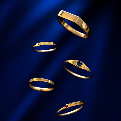 Five different 14k solid gold engravable bar rings against a dark blue background