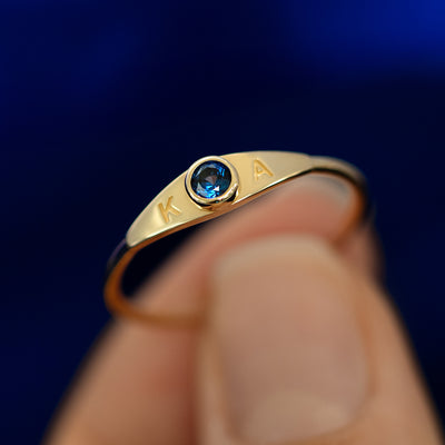 A model holding a gemstone monogram ring between two fingers to show the stone setting