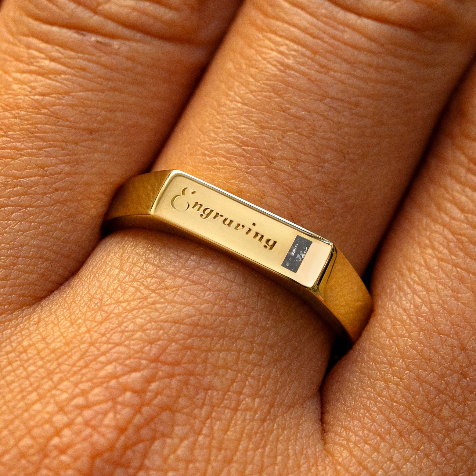 A model wearing a yellow gold baguette salt and pepper diamond rectangular signet ring with the word engraving on the top