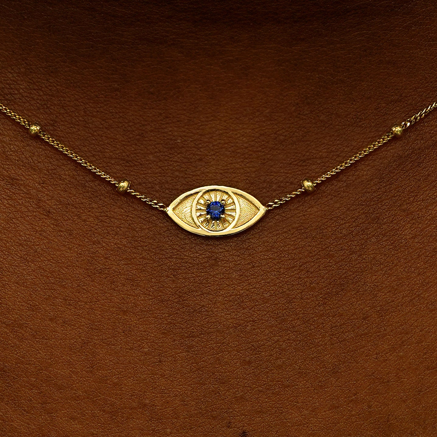 Close up view of a model's neck wearing a 14 karat gold sapphire evil eye necklace