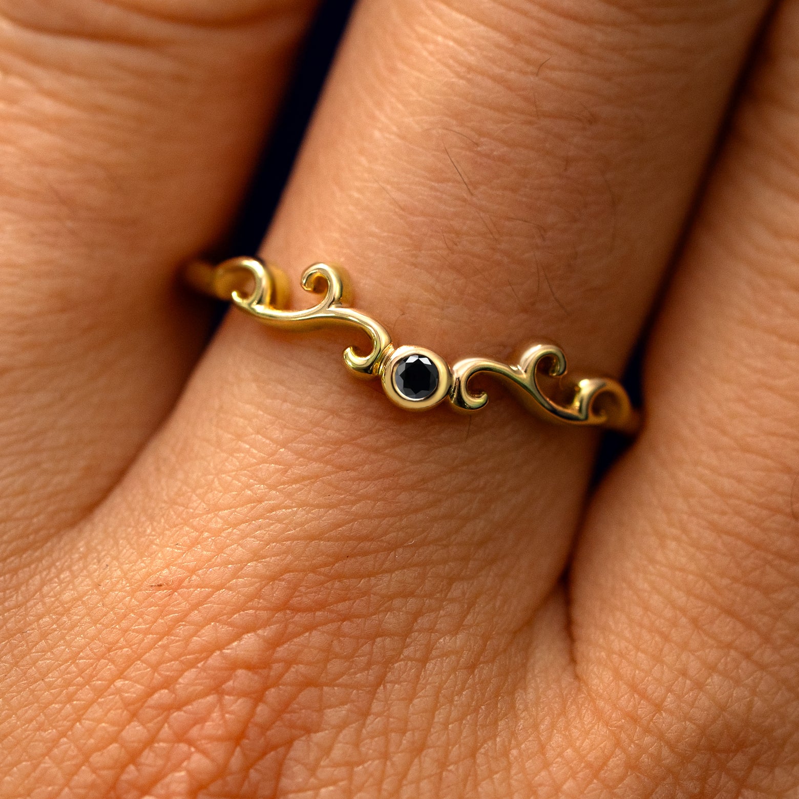 Close up view of a model's fingers wearing a 14k yellow gold Open Filigree Chevron Black Diamond Band