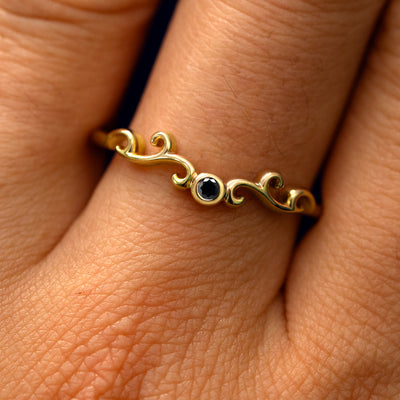 Close up view of a model's fingers wearing a 14k yellow gold Open Filigree Chevron Black Diamond Band