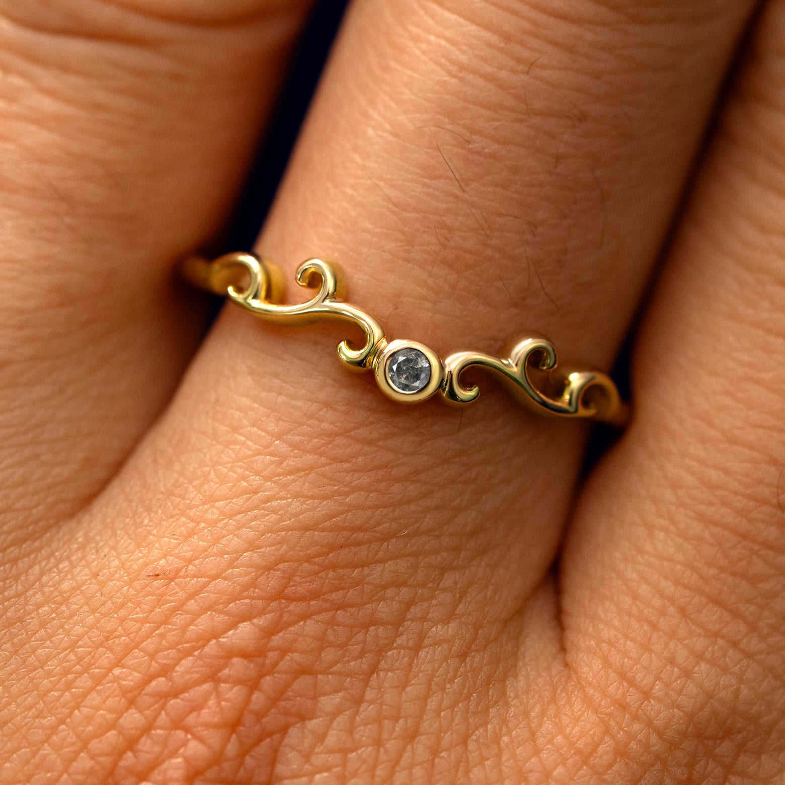 Close up view of a model's fingers wearing a 14k yellow gold Open Filigree Chevron Diamond Band