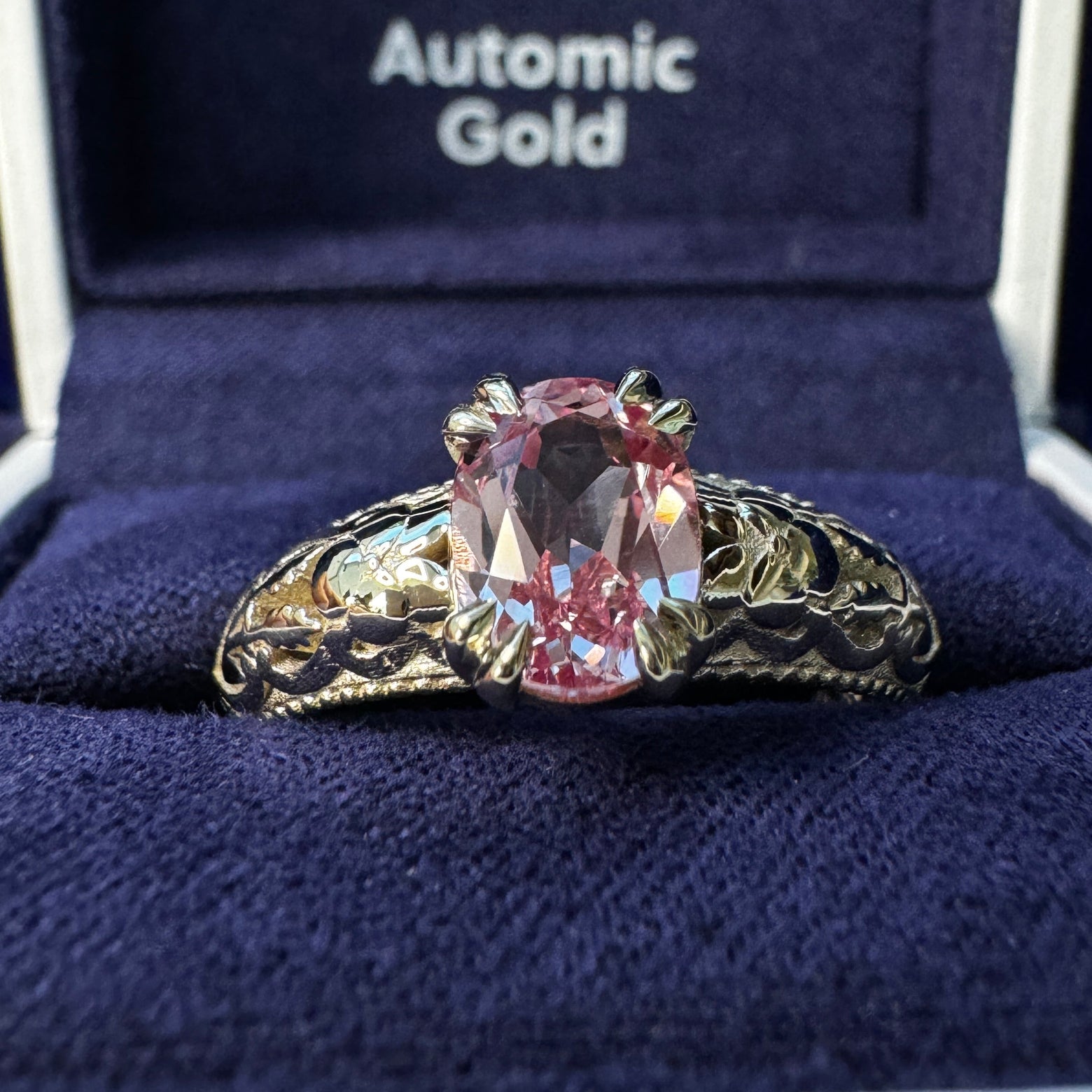 A photo of 14k Champagne Gold Double-claw-prongs-set 8x6mm Oval Peach-pink Lab Sapphire on Filigree Floral Milgrain Band Custom Ring in a blue ring box