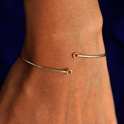 Close up view of a model's wrist wearing a 14k gold fire opal gemstone bypass bangle
