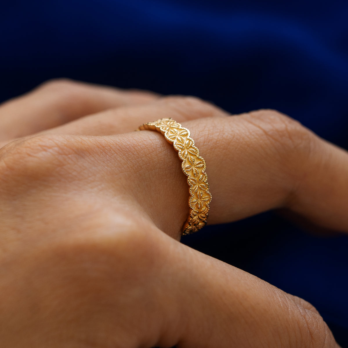 Side view of a model wearing a solid 14k yellow gold cowrie shell flower and rope band to show the raised engraving