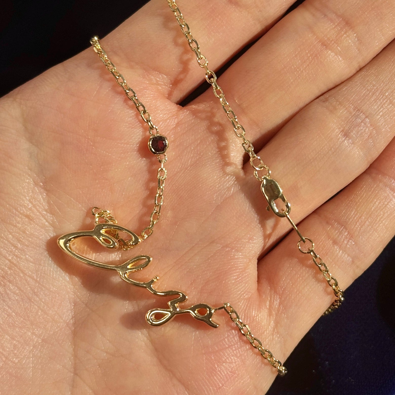18k Yellow Gold Garnet Charm w/ Nameplate ”Eliza” in Great Vibes Font on 16” Thick Cable Chain Custom Necklace resting on model's hand