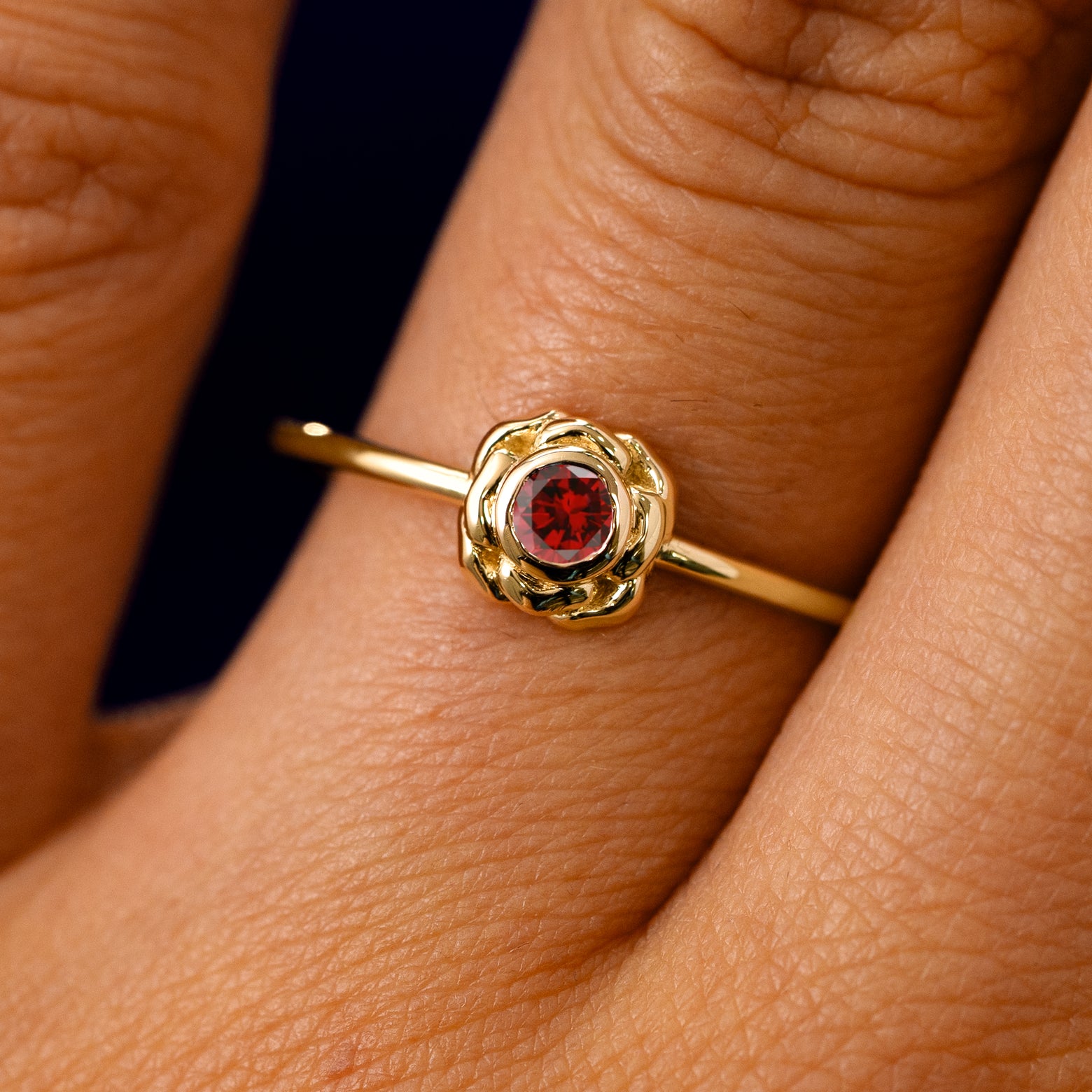 A solid 14k yellow gold Garnet Gemstone Flower Ring on a model's finger