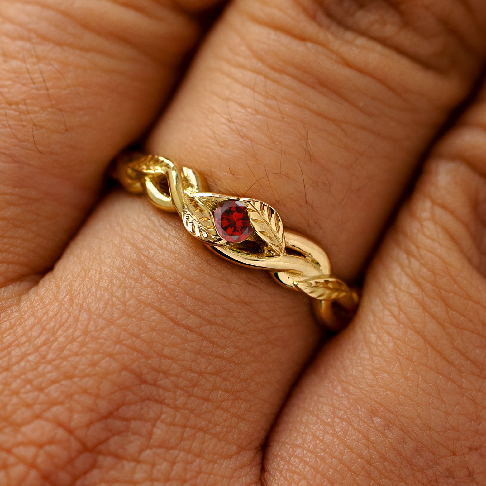A solid 14k yellow gold garnet leaves and vines ring on a model's finger