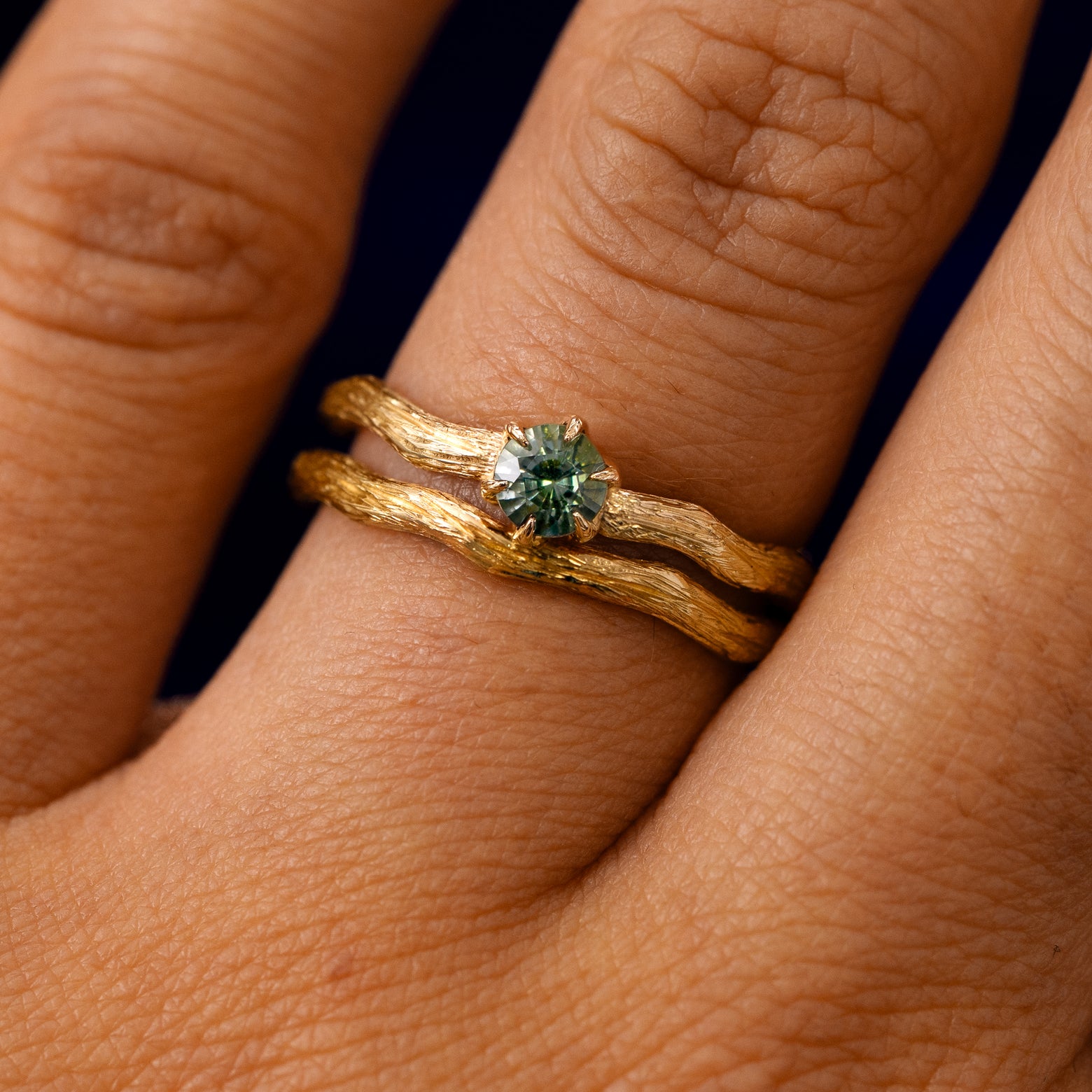 A model's fingers wearing a 14k yellow gold Montana Teal Sapphire Waved Branch Ring with Band