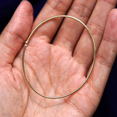 A yellow gold emerald clear diamond bypass bangle sitting in a model's palm to show the width of the bracelet