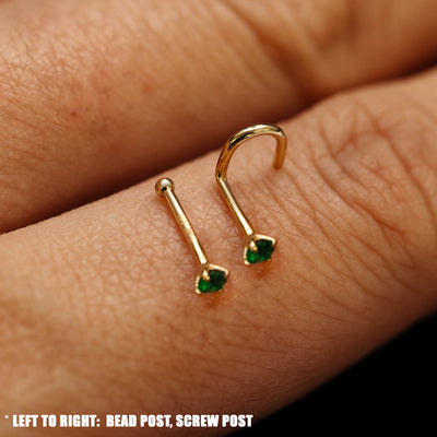 Close up view of 14k solid gold emerald Gemstone Nose Stud with bead post and screw post resting on the back on a model's hand