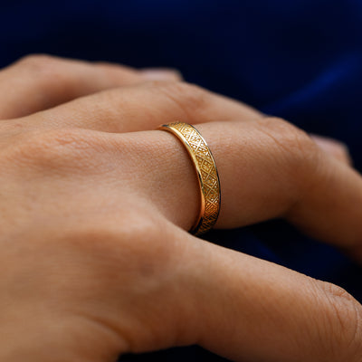 Side view of a model wearing a solid 14k yellow gold diamond patterned band to show the raised engraving