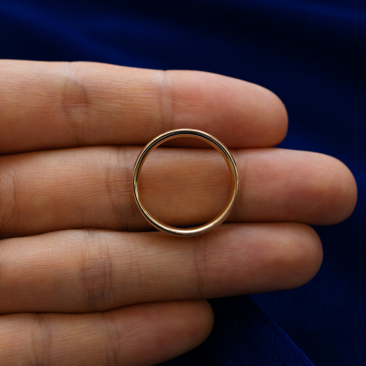 A diamond patterned band lying flat in a models hand to show the thickness of the ring