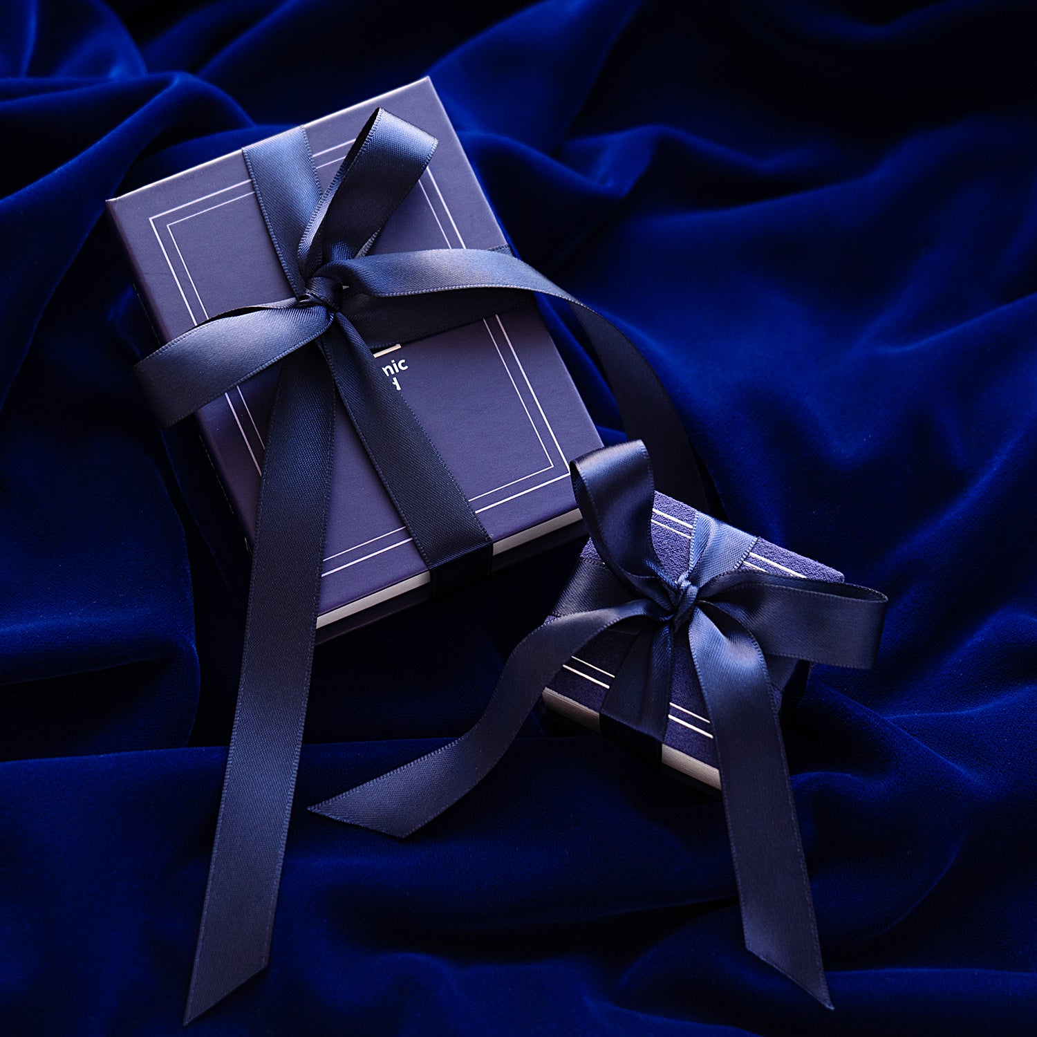 An Automic Gold Ring Box and Book Box both gift wrapped in a white ribbon that says Automic Gold in gold letters