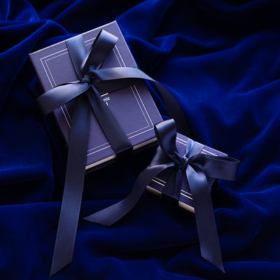 An Automic Gold Ring Box and Book Box both gift wrapped in a white ribbon that says Automic Gold in gold letters