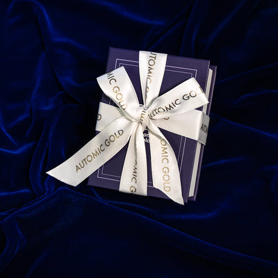 An Automic Gold Book Box gift wrapped with a white ribbon that says Automic Gold in gold letters