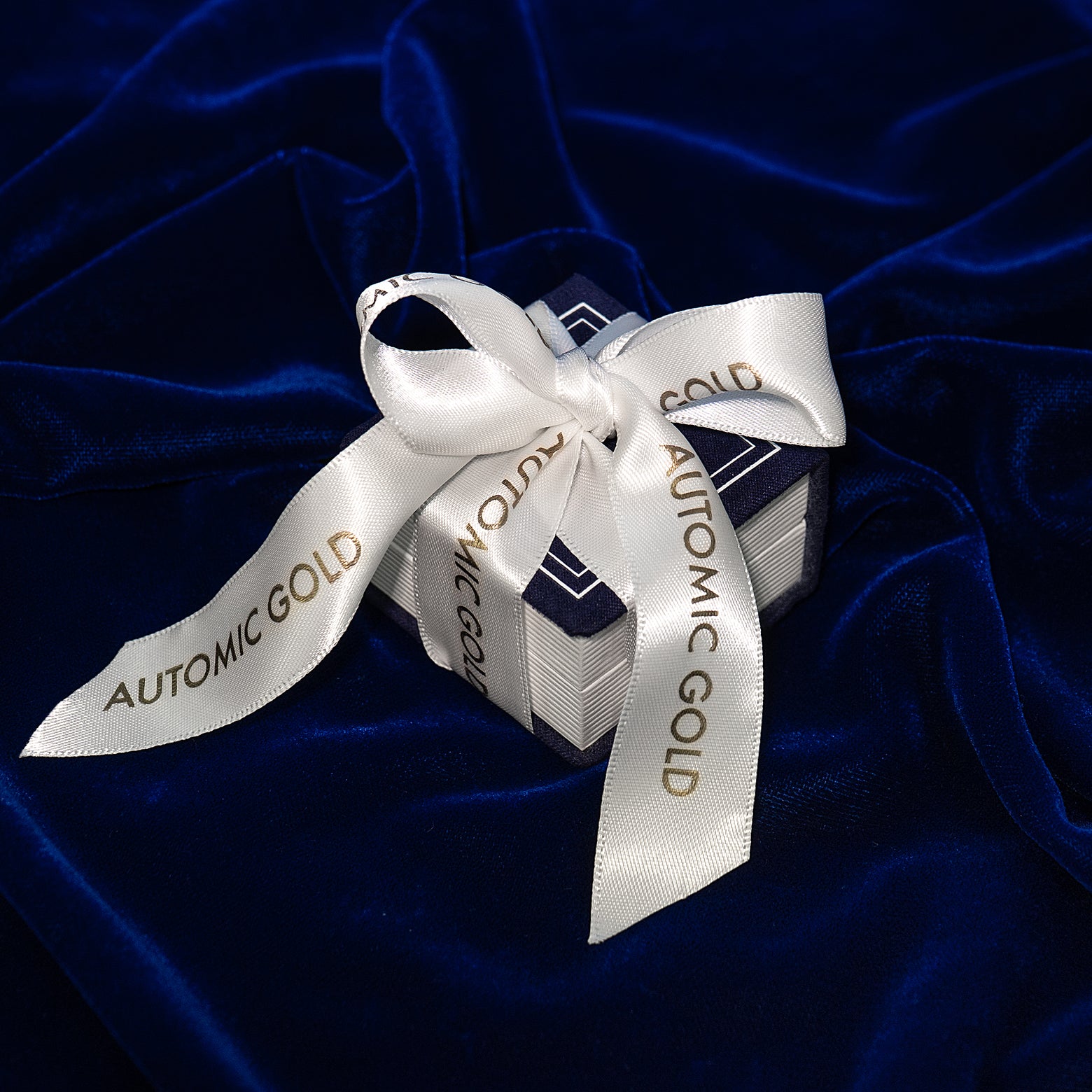 An Automic Gold Ring Box gift wrapped with a white ribbon that says Automic Gold in gold letters