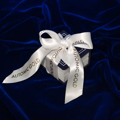 An Automic Gold Ring Box gift wrapped with a white ribbon that says Automic Gold in gold letters