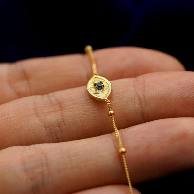 A 14k gold sapphire evil eye bracelet lying across a model's fingertips angled to show the setting and raised eye detailing