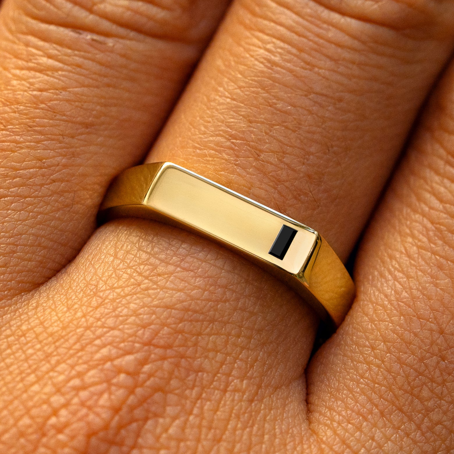 A model's finger wearing a yellow gold baguette black diamond rectangular signet ring