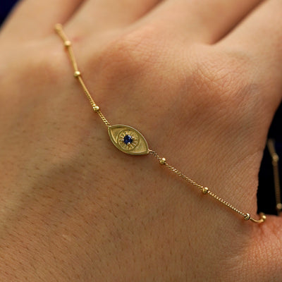 A solid gold gemstone evil eye bracelet draped across the back of a model's hand