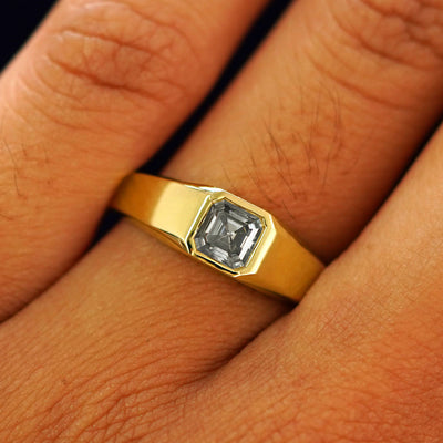 Close up view of a model's fingers wearing a yellow gold lab gray moissanite Asscher Gemstone Signet Ring