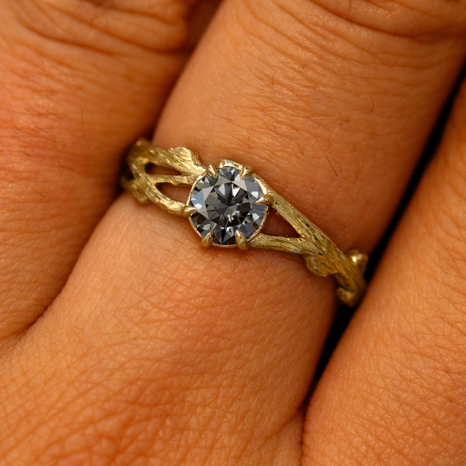 Close up view of a model's fingers wearing a 14k yellow gold Grey Moissanite Branches Ring